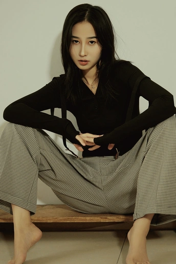 一位穿着黑色衬衫和长裙的年轻女子坐在长凳上