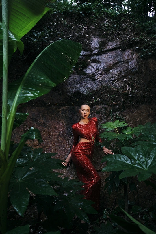 一位穿着红色连衣裙的女子在绿意盎然的森林中摆姿势 瀑布和绿色岩石环绕 