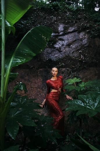 一位穿着红色连衣裙的女子在绿意盎然的森林中摆姿势 瀑布和绿色岩石环绕 