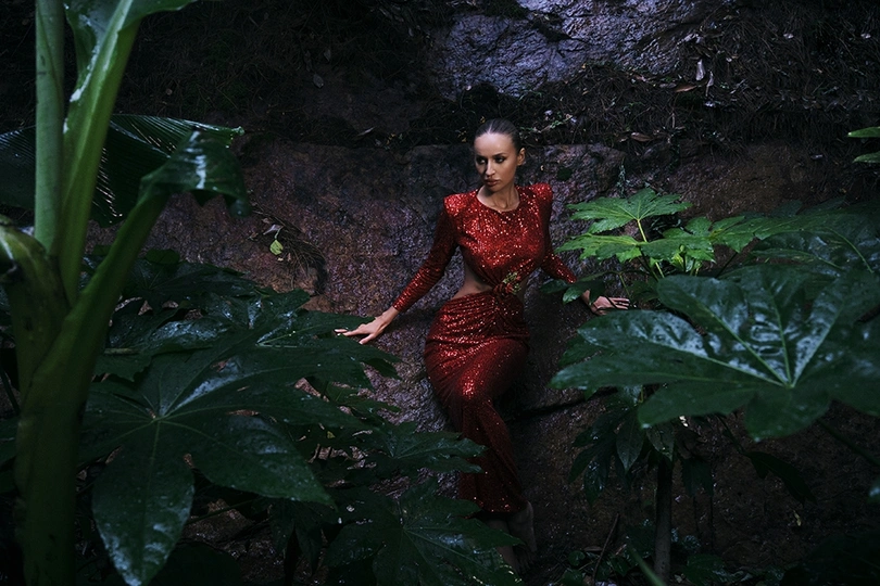 一个穿着红色连衣裙的女人站在一个黑暗的洞穴里 洞穴里有丛林中的植物。