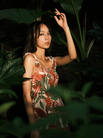 一位穿着连衣裙的年轻女子站在丛林中 背景中有植物。