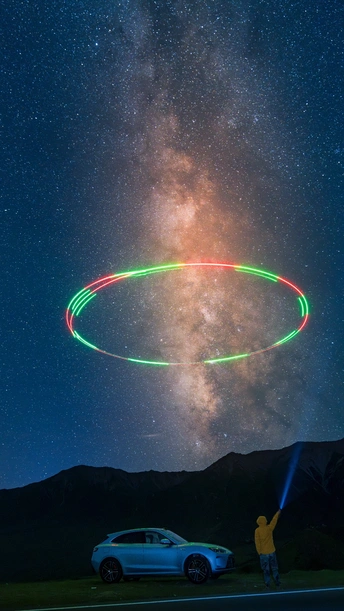 一个男子和他的汽车在天空中点亮了夜晚 形成了一个星星环。