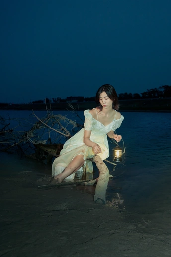 一个穿着白色连衣裙的年轻女子晚上提着灯笼坐在水中的海滩上