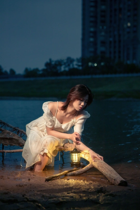 晚上 在海滩上 一个穿着白色连衣裙的年轻女子在水边的沙滩上点燃了一支小蜡烛