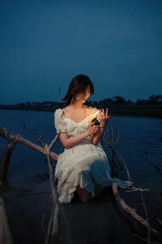 一个穿着白色连衣裙的年轻女子 手里拿着一支点燃的蜡烛 晚上坐在湖中