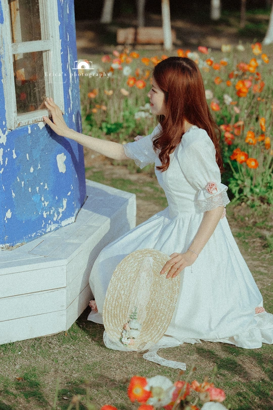 一个穿着白色连衣裙和草编帽子的年轻女子坐在靠近蓝色门的长椅上