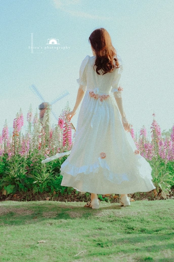 一位穿着白色连衣裙的年轻女子穿过一片花田
