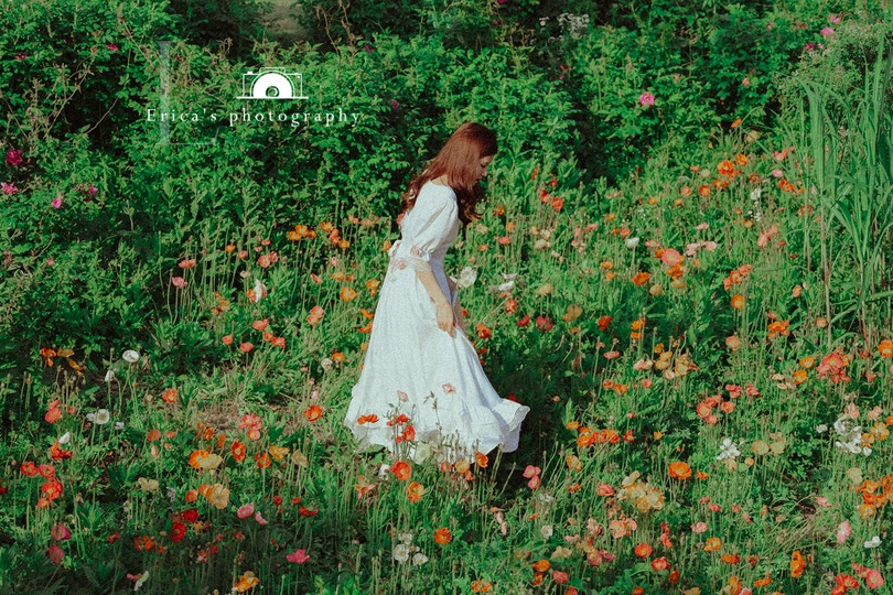 一位美丽的年轻女士穿着一件白色连衣裙站在野花丛中