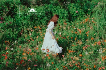 一位美丽的年轻女士穿着一件白色连衣裙站在野花丛中