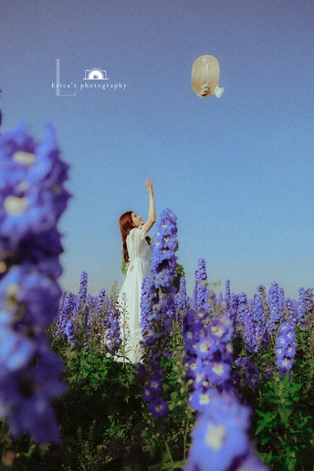 一个穿着白色连衣裙的年轻女子站在一片紫花丛中