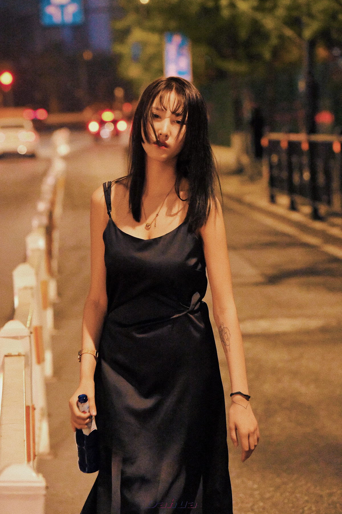 一个穿着黑色连衣裙的年轻女子在夜晚沿着人行道走