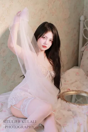 一个穿着白色连衣裙和面纱的年轻女子坐在床上