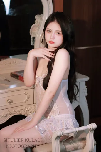 一个长发着白色连衣裙的年轻女子坐在镜子前的一把椅子上
