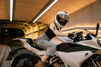 一个戴黑色头盔的男子坐在白色摩托车上 停在停车场