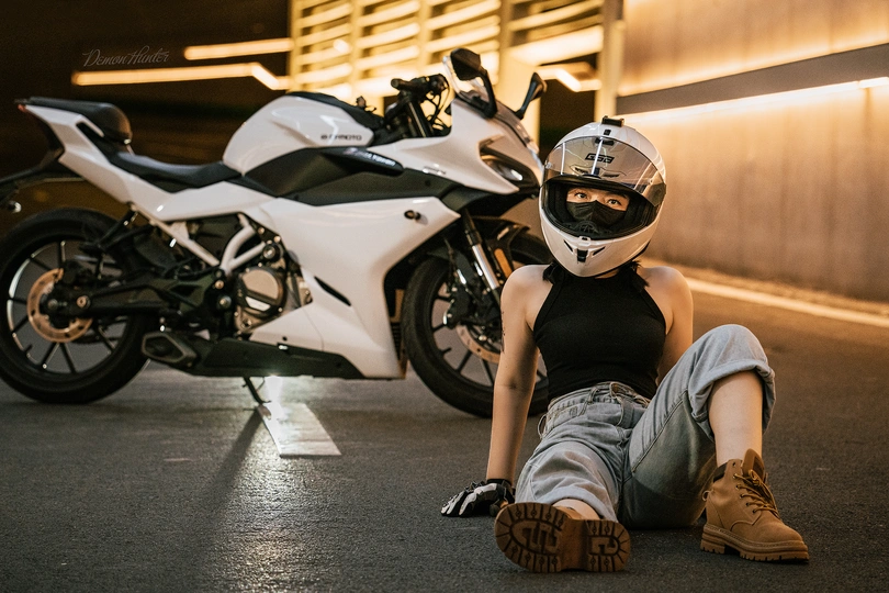 一个戴头盔的年轻男子躺在停车场的一辆白色摩托车旁边 一名女子坐在街上。