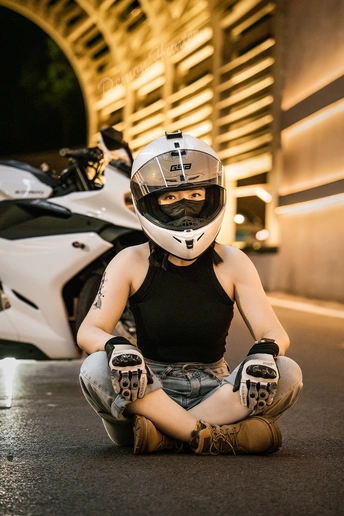 一个戴头盔的年轻男子坐在夜晚的一辆白色摩托车旁边