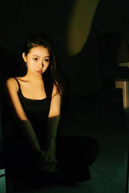 一个穿黑色衣服的女孩坐在一个黑暗的房间里 地板上有一盏绿色的灯。