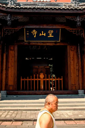 一位老人站在一座寺庙前面 背景有一栋建筑。