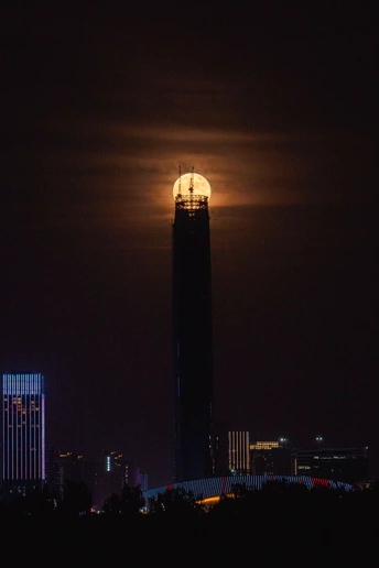 夜晚的城市上空 一轮满月照耀着 前景是一座高塔。