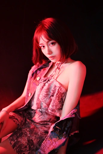 一个年轻女子穿着一件粉色的连衣裙坐在红色的雨伞下。