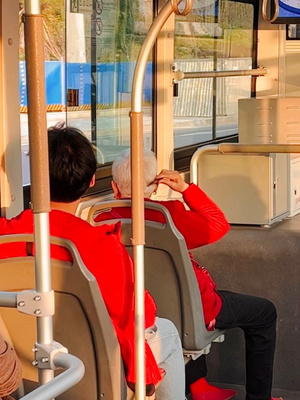 一个穿红夹克的男人坐在公交车上 其他人在座位上坐着。