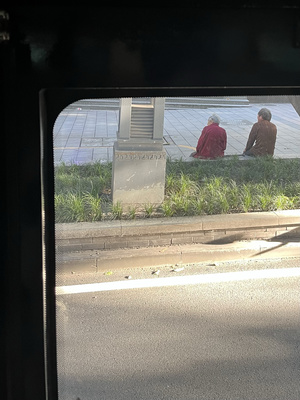 一个坐在人行道上的男人和一个坐在街道上的人 透过公共汽车窗户看到的景象