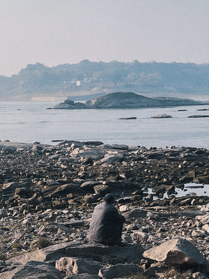 一位坐在岩石上 俯瞰水体或海洋的岸边男子。