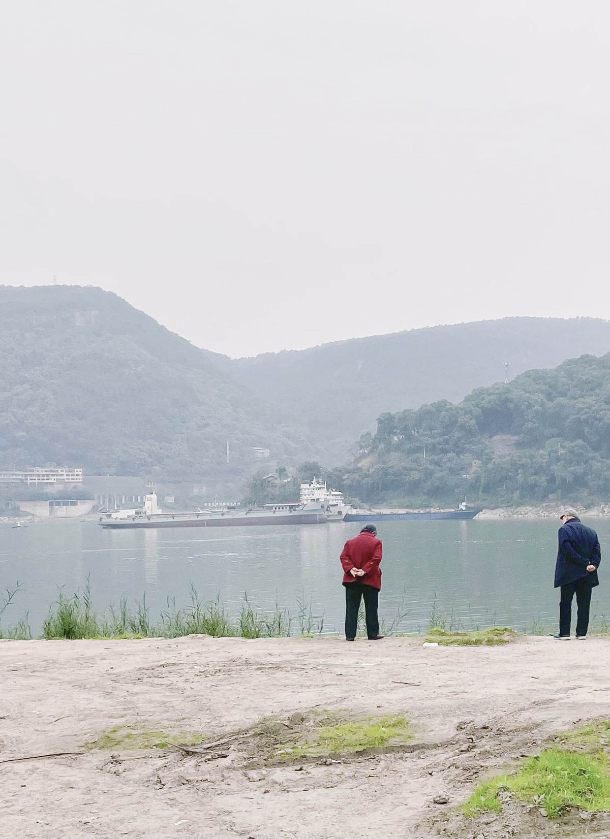 几名男子站在有山丘和船只远处的水边 手里拿着伞。